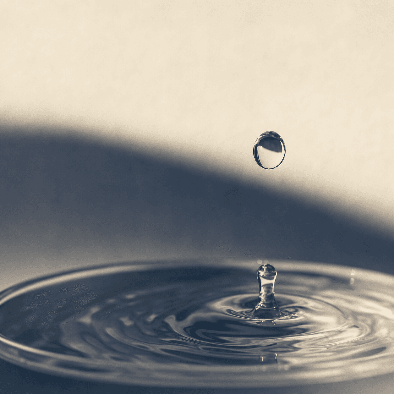 Macro water droplet above an indigo and cream brewing-water surface