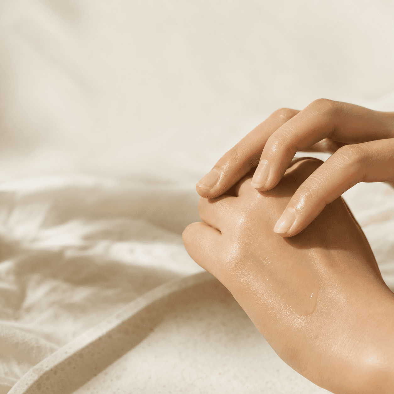 Hands pressing skincare essence into skin under warm muted light
